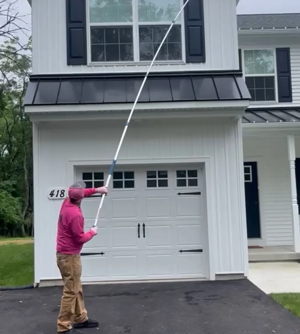 Technician using an extension wand to treat wasp nests under the eaves of a home