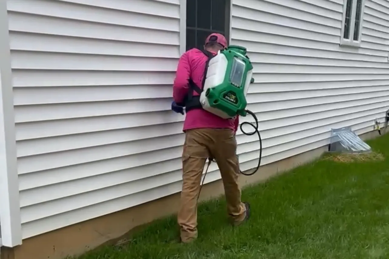 Technician applying a perimeter pest control treatment along a home foundation